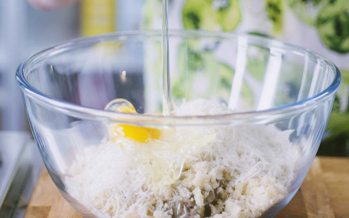 Uovo versato su formaggio grattugiato e mollica in una ciotola per le polpette di melanzane
