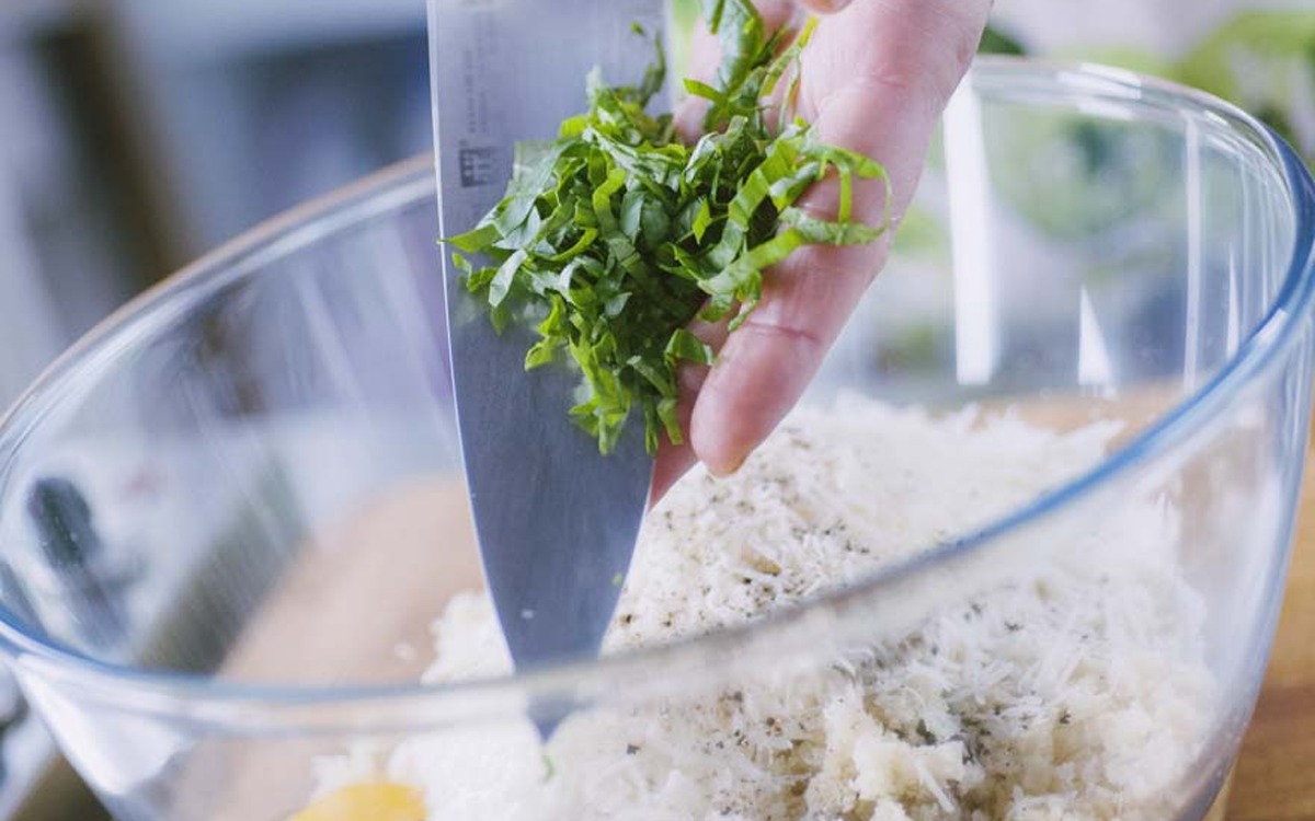 Basilico tagliato a striscioline aggiunto con un coltello all'impasto di pane grattugiato per le polpette di melanzane