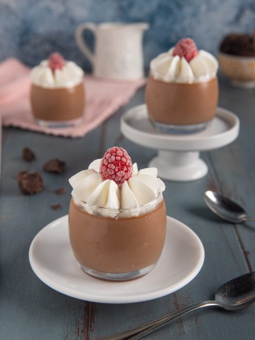 Cremoso al cioccolato in bicchiere con ciuffi di panna montata e un lampone fresco