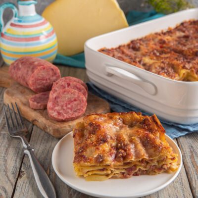 Lasagna con ragù di cotechino e fonduta gratinata in superficie, servita a fetta con cotechino affettato accanto