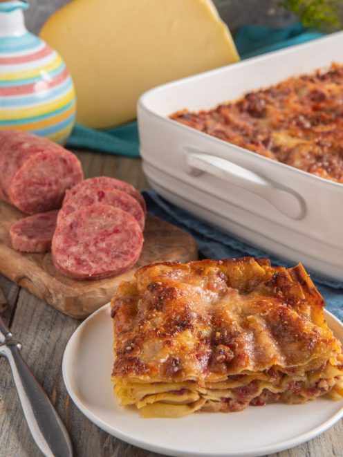 Lasagna con ragù di cotechino e fonduta gratinata in superficie, servita a fetta con cotechino affettato accanto