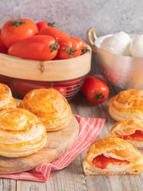 Rustici leccesi di pasta sfoglia dorata, uno aperto mostra il ripieno di pomodoro e mozzarella