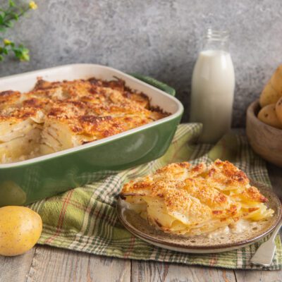 Patate alla romana gratinate con crosta dorata, servite a fette con strati di patate a fette