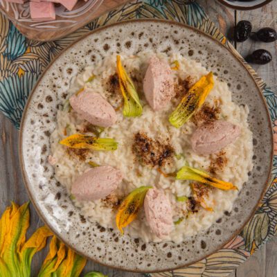Risotto con mortadella e mascarpone guarnito con fiori di zucca e polvere di olive nere