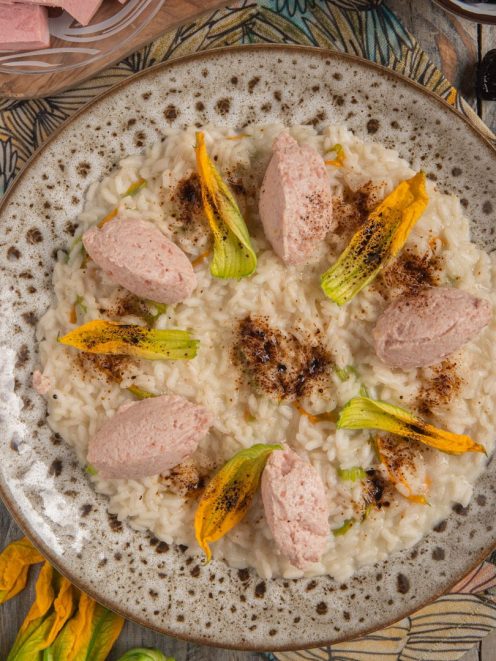 Risotto con mortadella e mascarpone guarnito con fiori di zucca e polvere di olive nere