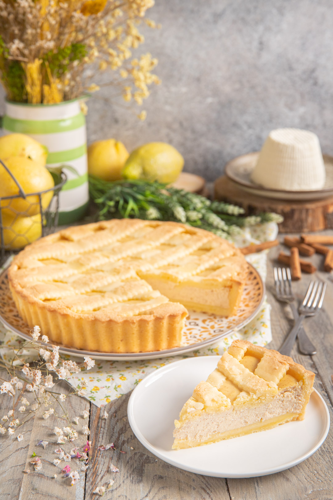 Fetta di crostata di ricotta con pasta frolla a griglia dorata, accanto alla torta intera