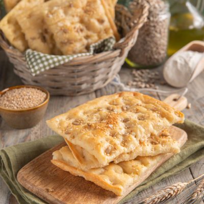 Focaccia croccante ai semi di sesamo e girasole impilata su tagliere di legno
