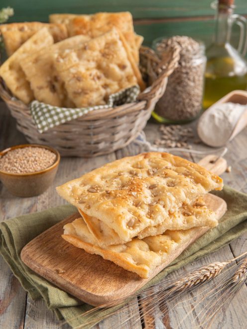 Focaccia croccante ai semi di sesamo e girasole impilata su tagliere di legno