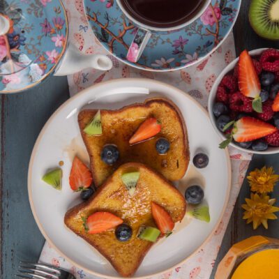 French toast dorato con sciroppo, fragole, mirtilli e kiwi accanto a una ciotola di frutti di bosco