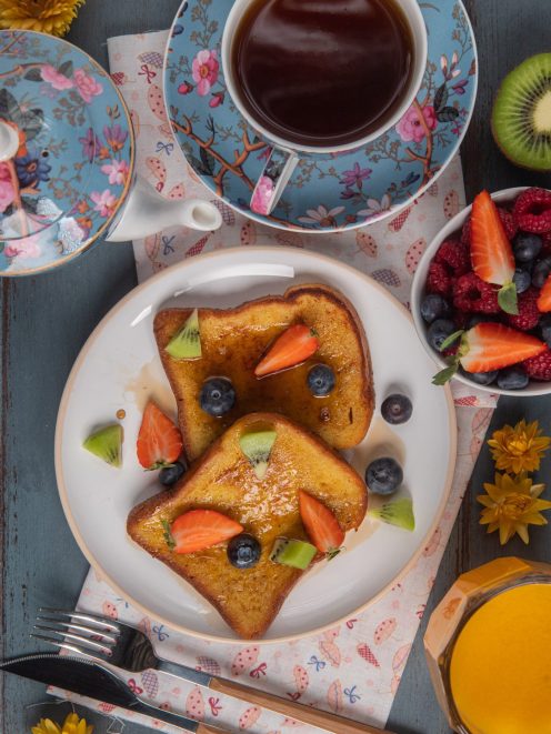 French toast dorato con sciroppo, fragole, mirtilli e kiwi accanto a una ciotola di frutti di bosco