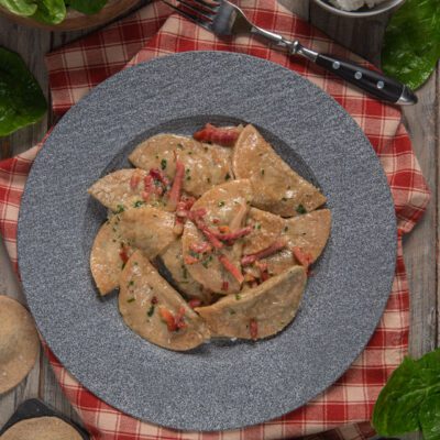 Schlutzkrapfen con speck conditi con salsa cremosa, pezzetti di speck e prezzemolo tritato