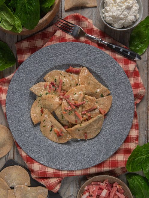 Schlutzkrapfen con speck conditi con salsa cremosa, pezzetti di speck e prezzemolo tritato