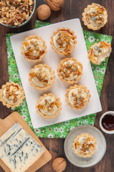 Tartellette al gorgonzola con gocce di miele e granella di noci su vassoio