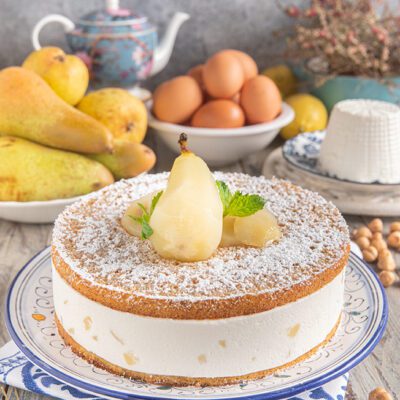 Torta di ricotta e pere spolverata di zucchero a velo con una pera intera e foglie di menta
