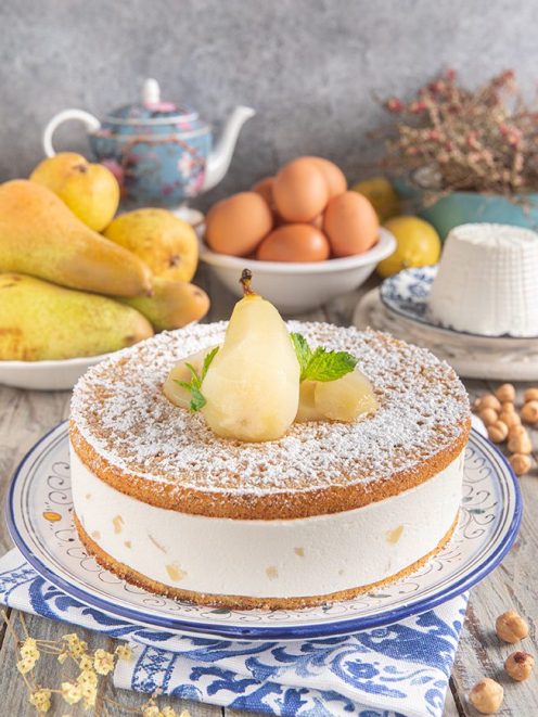 Torta di ricotta e pere spolverata di zucchero a velo con una pera intera e foglie di menta