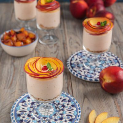 Cheesecake in bicchiere con base di biscotto, crema alla pesca e rose di nettarine fresche