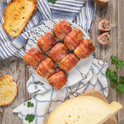 Bombette pugliesi avvolte nella pancetta e infilzate su spiedini, servite con formaggio e pane tostato