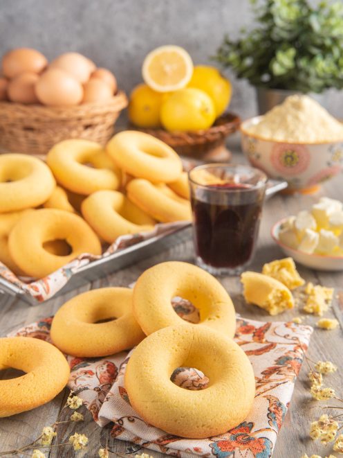 Ciambelline d'Aosta appena sfornate impilate accanto a limoni, uova e un bicchiere di vino rosso