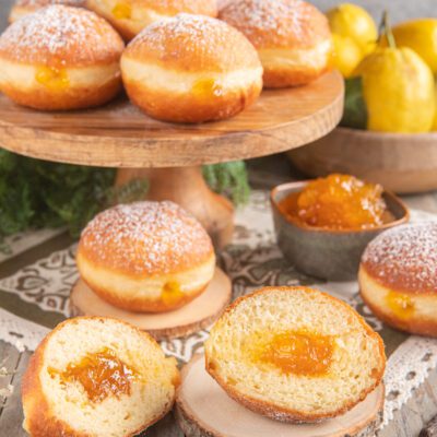 Krapfen soffici spolverati di zucchero a velo, farciti con marmellata all'albicocca, uno tagliato a metà