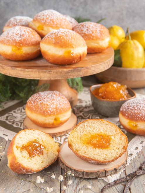 Krapfen soffici spolverati di zucchero a velo, farciti con marmellata all'albicocca, uno tagliato a metà