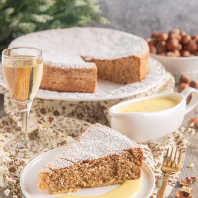 Torta di nocciole delle Langhe con zabaione al moscato, una fetta servita con crema accanto alla torta intera