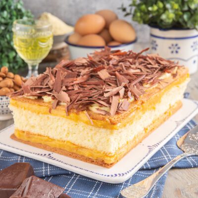 Torta pazientina a strati di pan di spagna e crema pasticcera coperta di scaglie di cioccolato