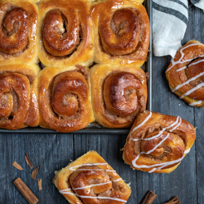 Cinnamon roll dorati appena sfornati, con glassa bianca a filo e stecche di cannella accanto