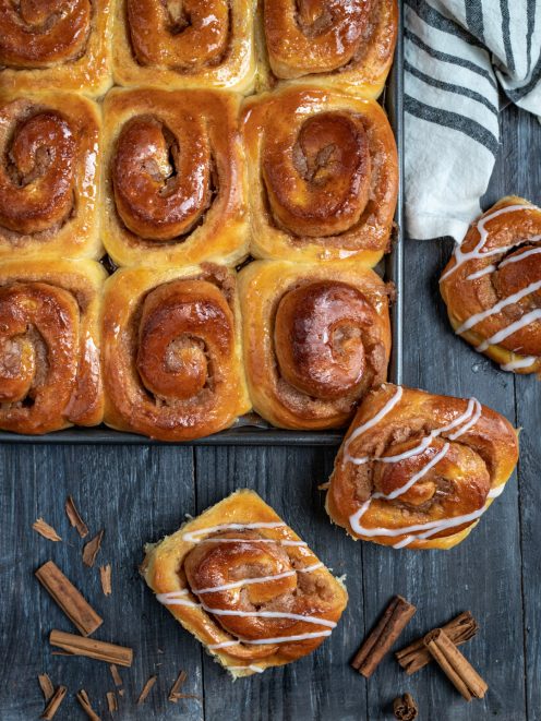 Cinnamon roll dorati appena sfornati, con glassa bianca a filo e stecche di cannella accanto