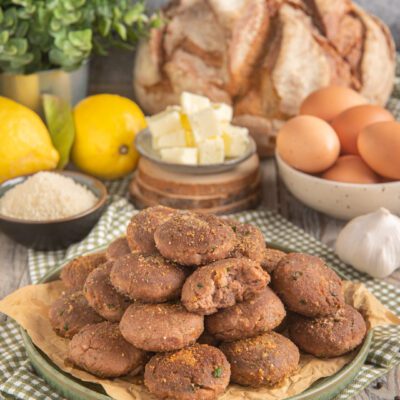 Mondeghili impilati su carta da forno, con pangrattato in superficie e aglio sullo sfondo