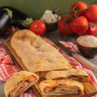 Rotolo di pizza alla parmigiana tagliato a fette che mostrano il ripieno filante di melanzane e pomodoro