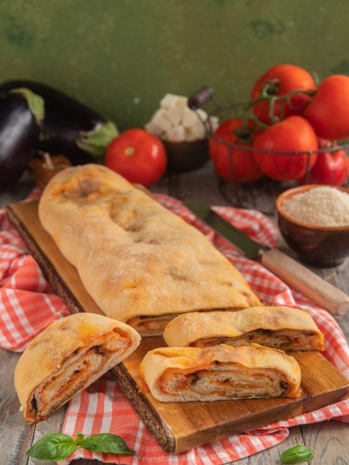 Rotolo di pizza alla parmigiana tagliato a fette che mostrano il ripieno filante di melanzane e pomodoro