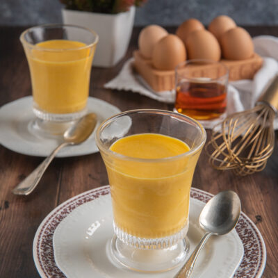 Zabaione cremoso servito in bicchieri da dessert, con uova fresche sullo sfondo