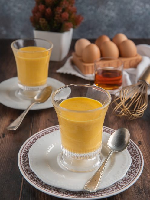 Zabaione cremoso servito in bicchieri da dessert, con uova fresche sullo sfondo