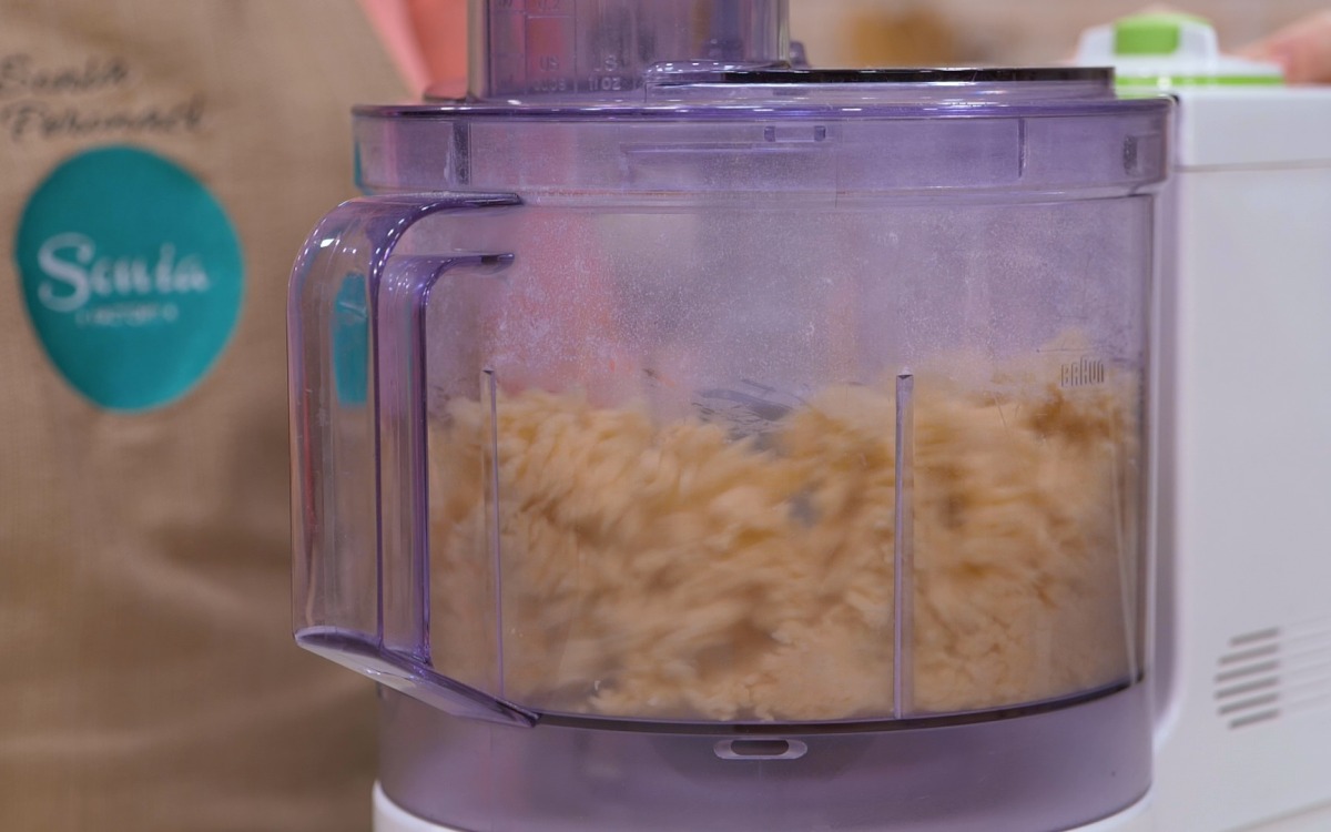 Impasto di pasta frolla appena formato nel robot da cucina, ancora granuloso e compatto