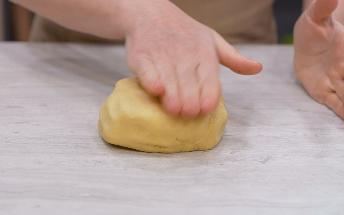Mani che compattano un panetto di pasta frolla sul piano di lavoro