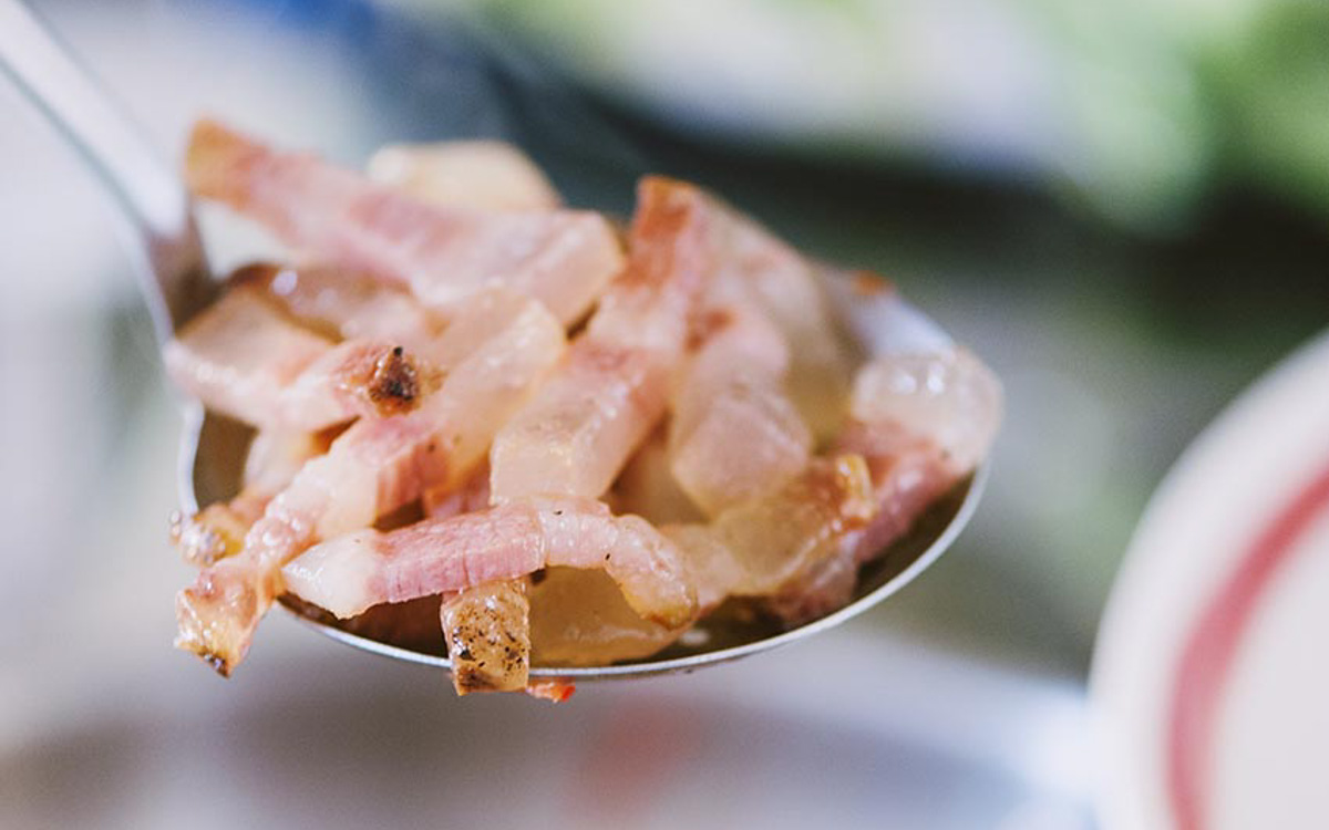Striscioline di guanciale rosolato sollevate con un cucchiaio, con il grasso ancora lucido