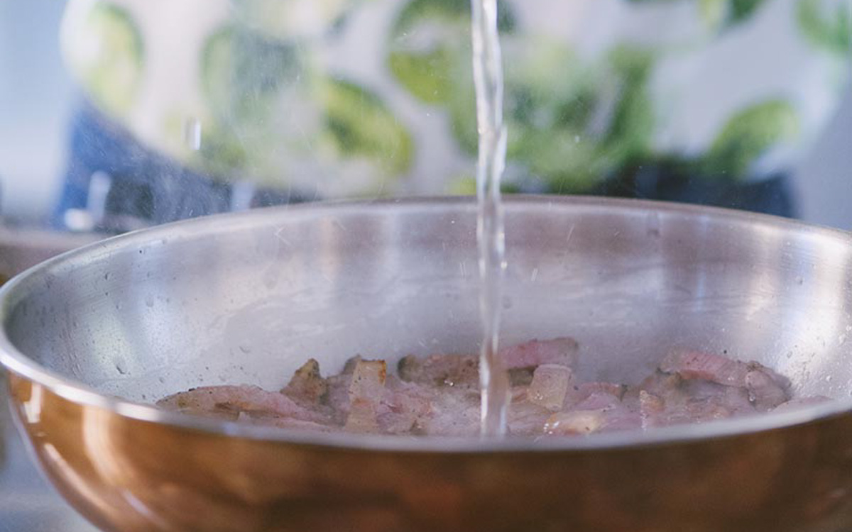 Vino bianco versato sul guanciale rosolato in padella durante la preparazione dell'amatriciana