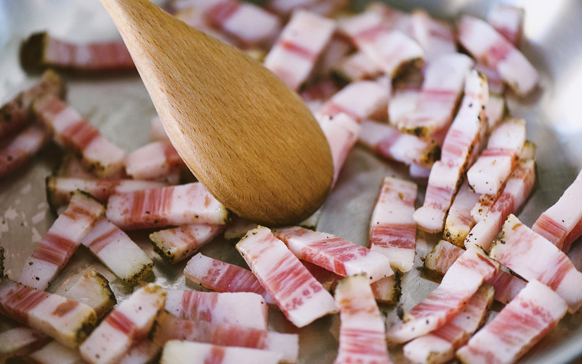 Cubetti di guanciale che rosolano in padella, mescolati con un cucchiaio di legno