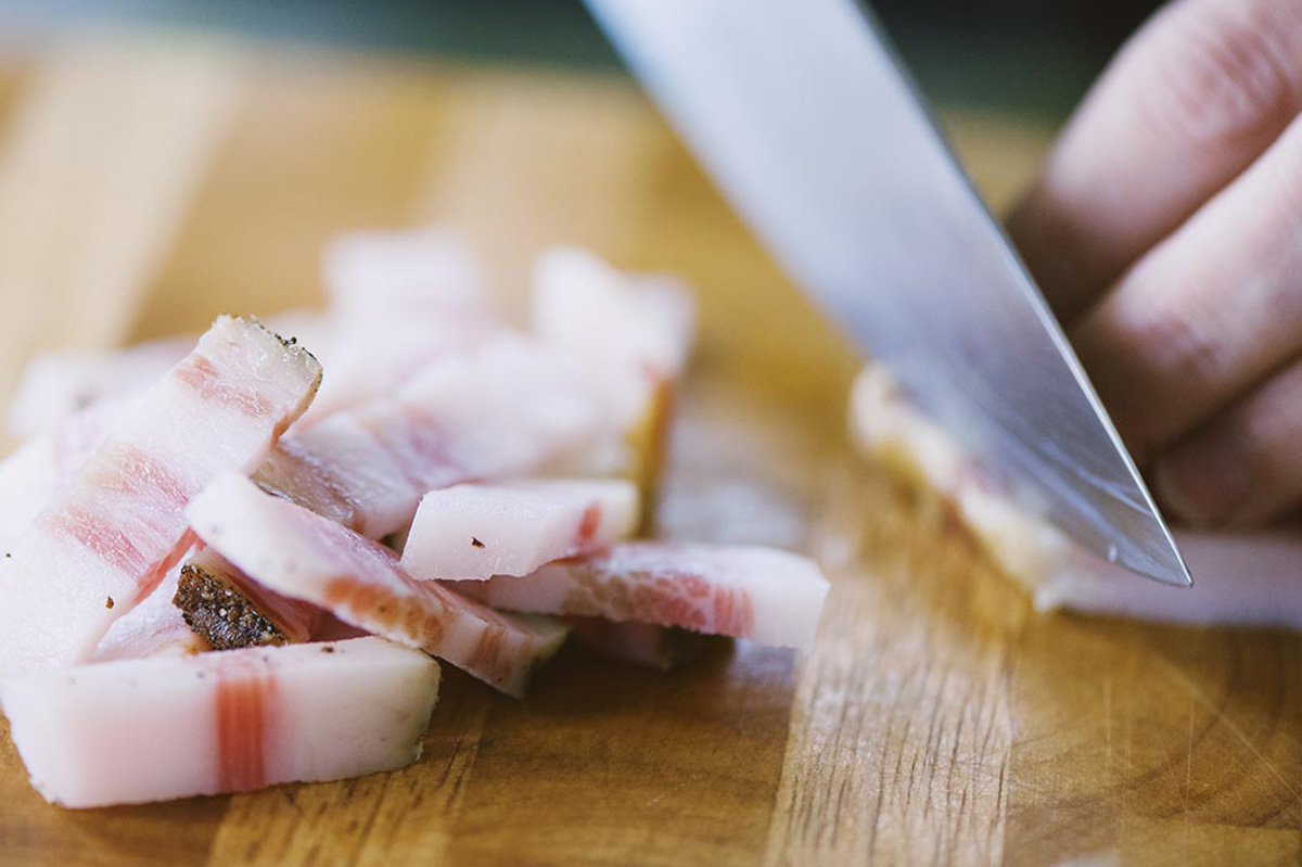 Guanciale tagliato a listarelle con un coltello sul tagliere