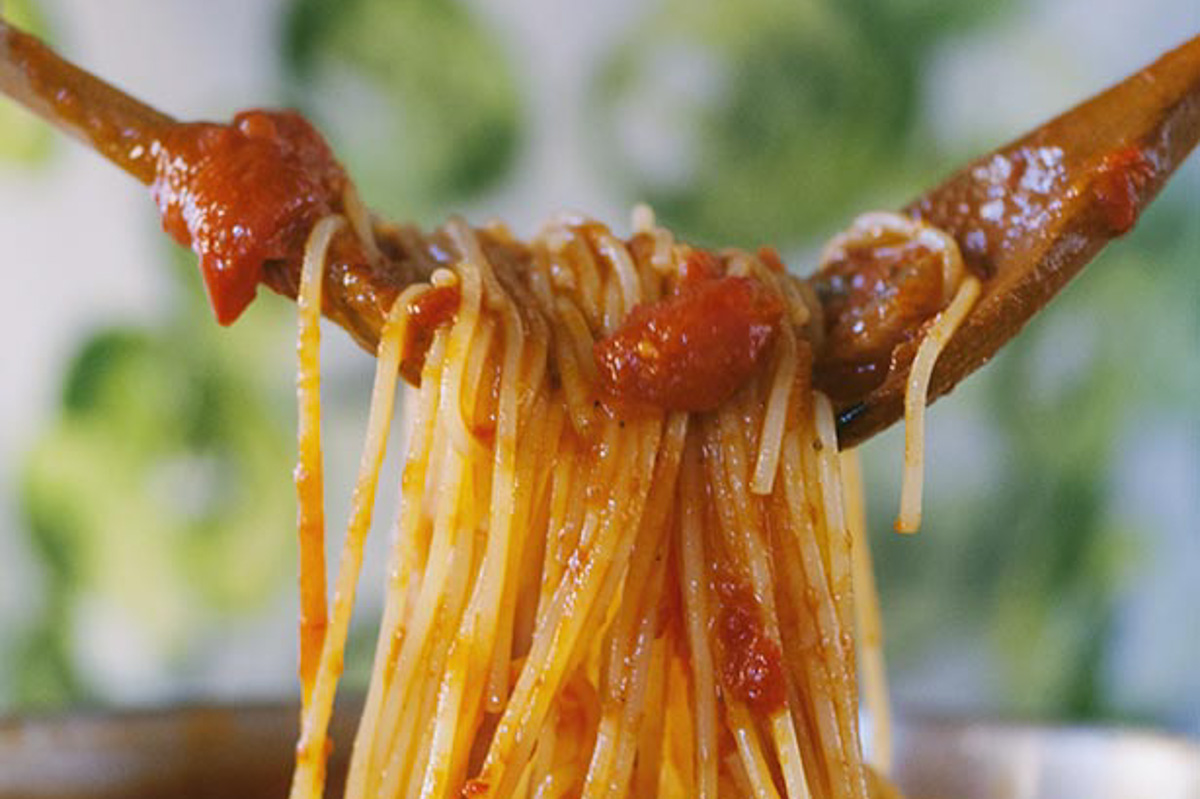 Spaghetti all'amatriciana sollevati con due forchette, ricoperti di sugo di pomodoro e guanciale