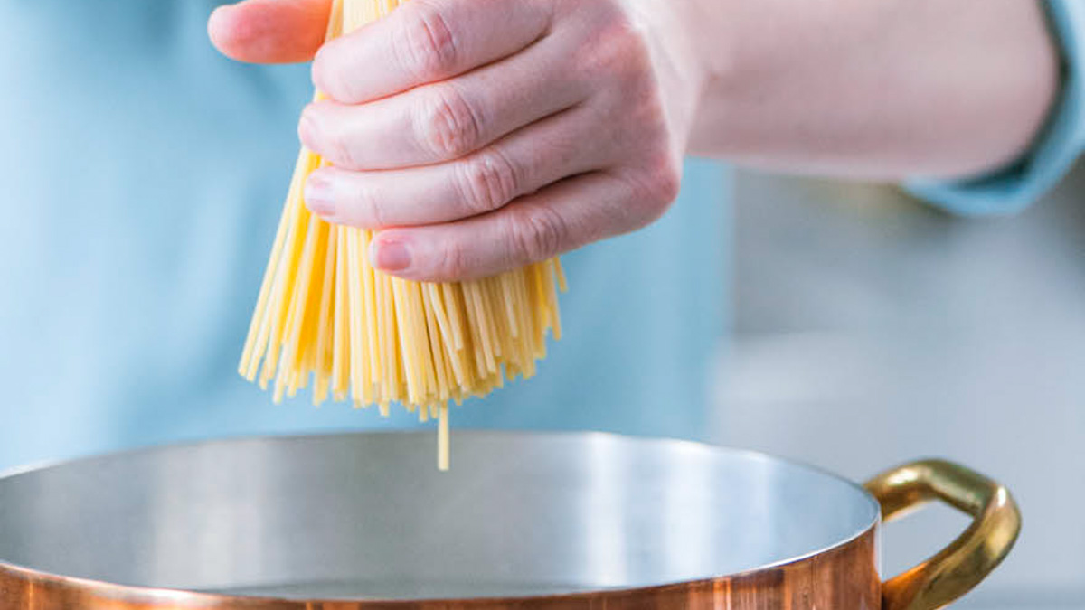 Mano che cala gli spaghetti crudi nell'acqua della pentola