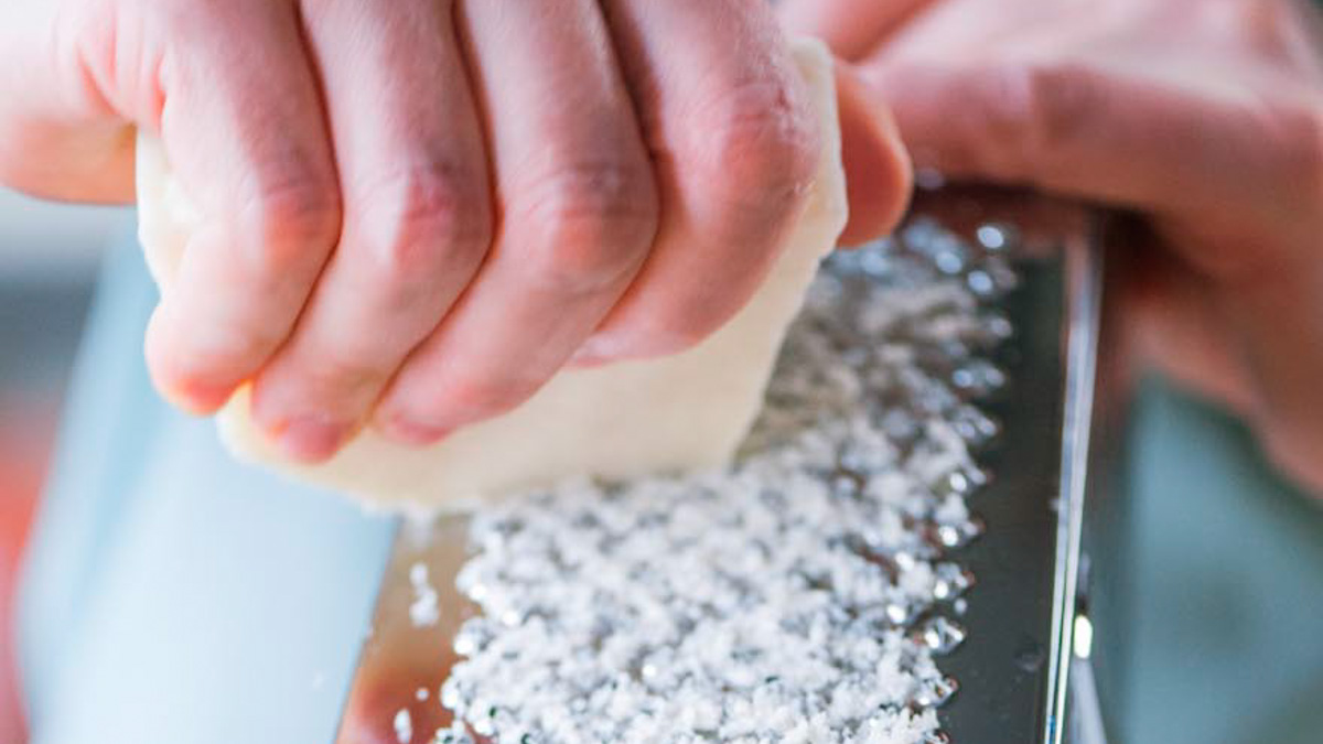 Mani che grattugiano finemente il pecorino sulla grattugia