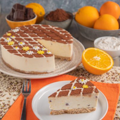 Cheesecake alla stracciatella e arancia con cacao in polvere a scacchi e fiorellini di zucchero, servita a fetta