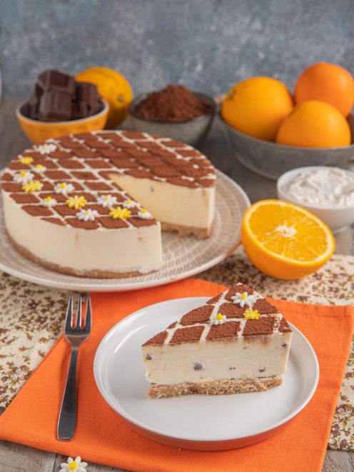 Cheesecake alla stracciatella e arancia con cacao in polvere a scacchi e fiorellini di zucchero, servita a fetta