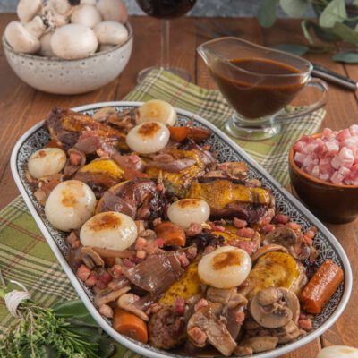 Coq au vin con funghi champignon, cipolline dorate, pancetta e carote in salsa al vino rosso