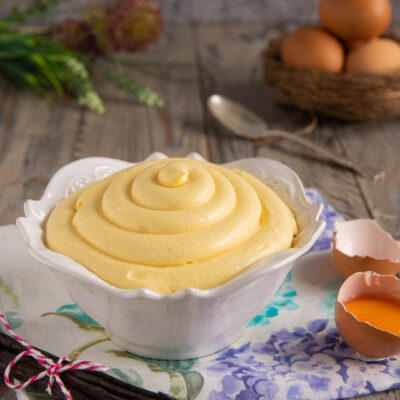 Crema pasticcera densa e vellutata servita a spirale, con baccelli di vaniglia e guscio d'uovo accanto