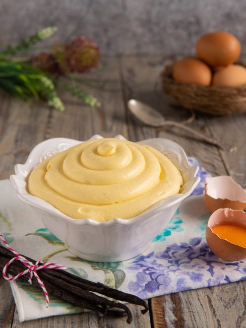Crema pasticcera densa e vellutata servita a spirale, con baccelli di vaniglia e guscio d'uovo accanto