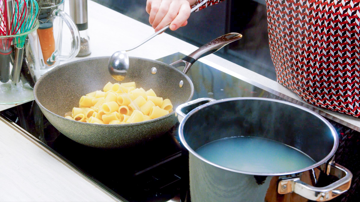 Rigatoni trasferiti in padella con un mestolo di acqua di cottura versata dalla pentola accanto