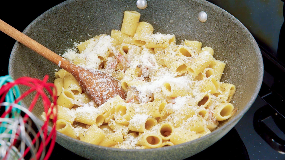 Rigatoni alla gricia mantecati in padella con pecorino grattugiato e guanciale, mescolati con cucchiaio di legno