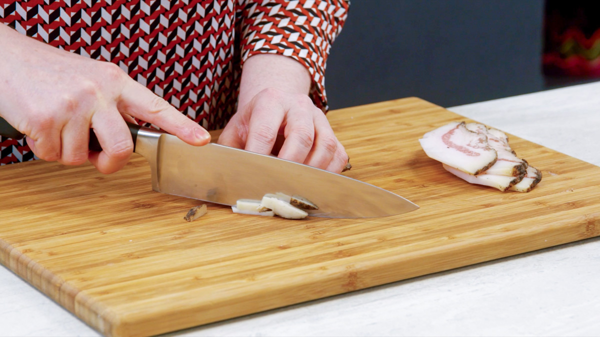 Mani che tagliano il guanciale a listarelle sul tagliere
